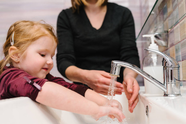Washing hands. Stop spreading coronavirus. Preventive measures against Covid-19 infection. Mom tells child how to wash her hands with antibacterial soap properly, warm water rubbing nails and fingers. - Фото, изображение