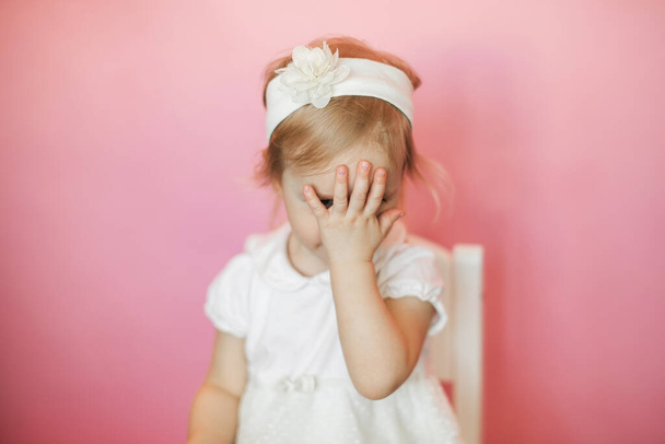 little girl in a white dress covers her face with her hand - Fotografie, Obrázek