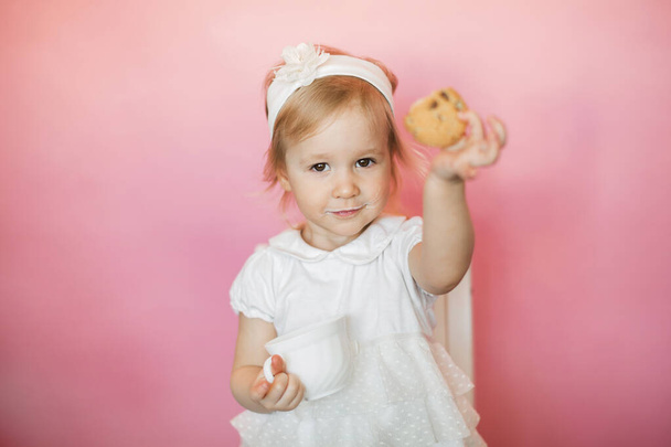 little girl has breakfast, eats cookies and drinks kefir from a cup - Photo, Image