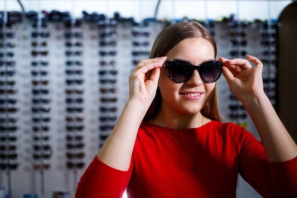 mooi jong meisje kiest zonnebril in een optiek winkel. - Foto, afbeelding