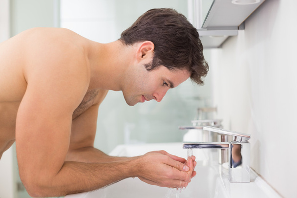 Side view of shirtless man washing face in bathroom - Photo, image