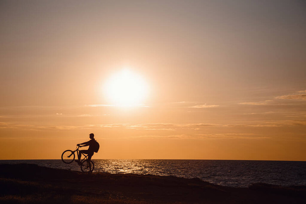 Silhouette des Radfahrers in Bewegung bei schönem Sonnenuntergang. Idee und Konzept eines gesunden Lebensstils, Bewegung für die Gesundheit und Ausnahmeregelungen in Quarantäne - Foto, Bild