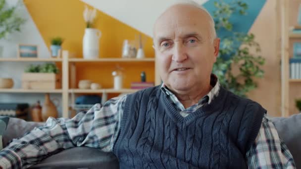 Πορτρέτο του ανέμελος γέρος κάθεται στον καναπέ στο σπίτι χαμογελώντας κοιτάζοντας κάμερα - Πλάνα, βίντεο