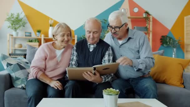 Group of elderly people watching photos in album talking sitting on couch at home - Filmagem, Vídeo