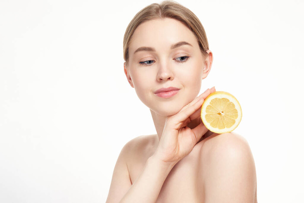Young attractive girl posing at studio with lemon. Beautiful female face with healthy skin and eyes. Young blonde natural woman with vivid makeup. Skin care. Vitamin C - Фото, изображение