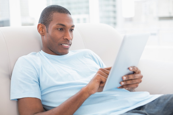 Side view of casual Afro man using digital tablet on sofa - Fotoğraf, Görsel