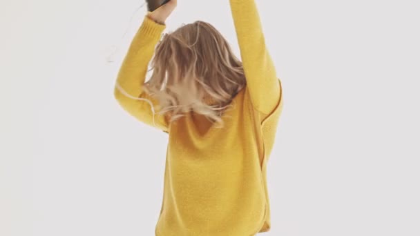 Happy pretty blonde woman in sweater listening music and dancing over grey background - Felvétel, videó