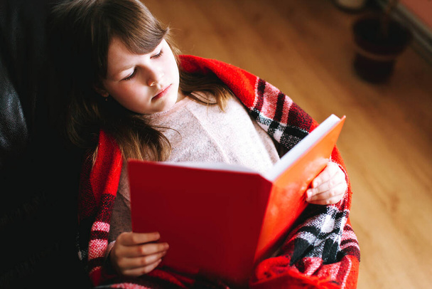 Mädchen beim Lesen eines Buches, das während der Quarantäne auf der Couch liegt. Bleiben Sie zu Hause, um die Ausbreitung des Coronavirus zu stoppen - Foto, Bild
