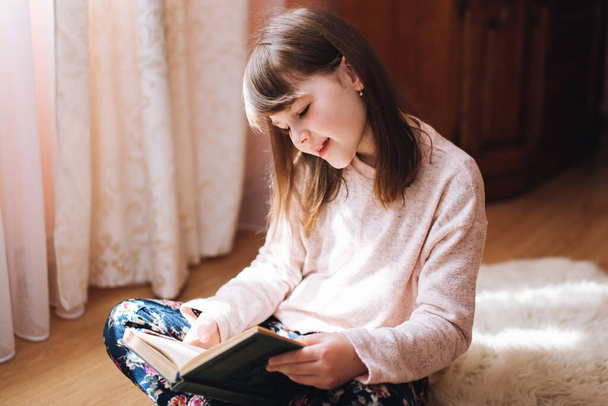 Κορίτσι που διαβάζει ένα βιβλίο, διασκεδάζει στο σπίτι κατά τη διάρκεια της καραντίνας. - Φωτογραφία, εικόνα