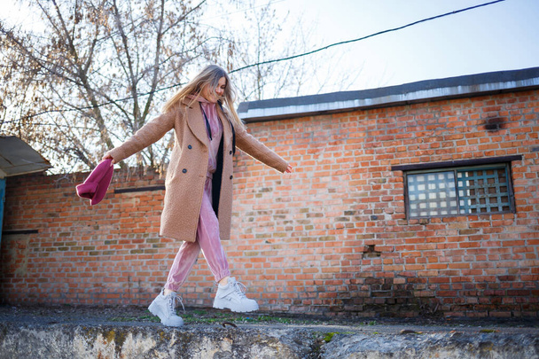 modello ragazza elegante in un cappotto marrone, abito rosa e stivali grigi sulle rovine della città. Le tendenze della moda moderna. Immagine alla moda
 - Foto, immagini