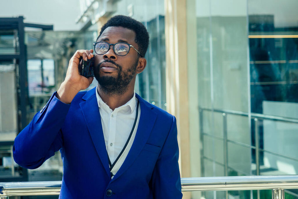 Young afro businessman in blue suit stands in office looks through big window at the city in airport terminal - Foto, Imagen