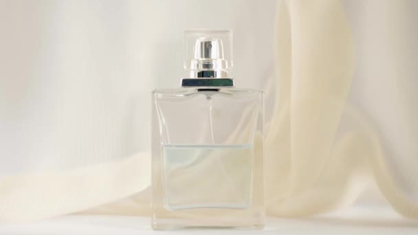 Na bílém stole je plochá lahvička s azurovým parfémem nebo esenciálními oleji. Béžová tkanina se třepotá a mává ve vzduchu kolem láhve. Pojem aroma a vůně. Zavřít. Zpomalený pohyb - Záběry, video