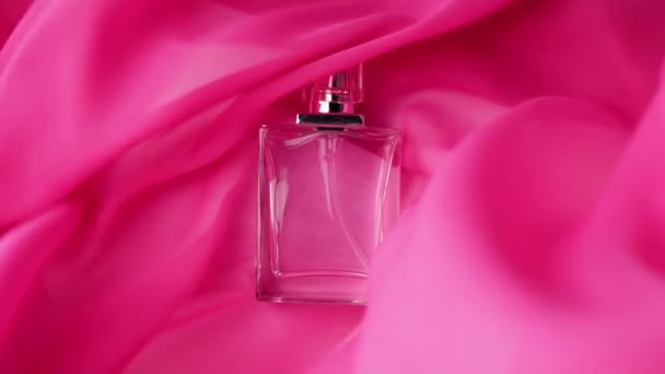 Lapos felületű palack cián parfümök vagy illóolajok a rózsaszín ruhán. Rózsaszín szövet repked és integet az üveg körül. Fogalom az aromáról és a szagról. Közelről. Lassú mozgás. - Felvétel, videó