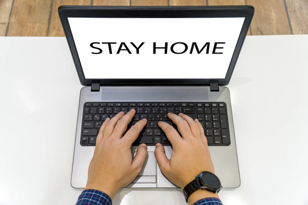 Pohled shora na osobu pracující na notebooku se zprávou zůstat doma na obrazovce - Fotografie, Obrázek