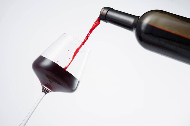 Lahvička červeného vína nalitá do sklenice na bílém pozadí.  - Fotografie, Obrázek