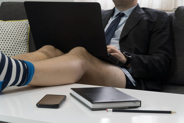 Work from home concept. Businessman having a conference call on a laptop with no pants and his legs on the table - Fotoğraf, Görsel
