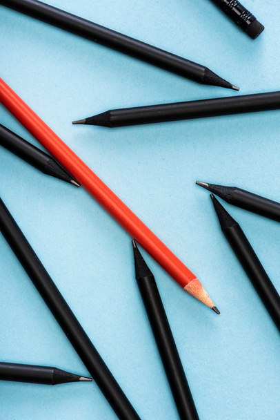 Top view of unique red pencil among black on blue background - Fotoğraf, Görsel