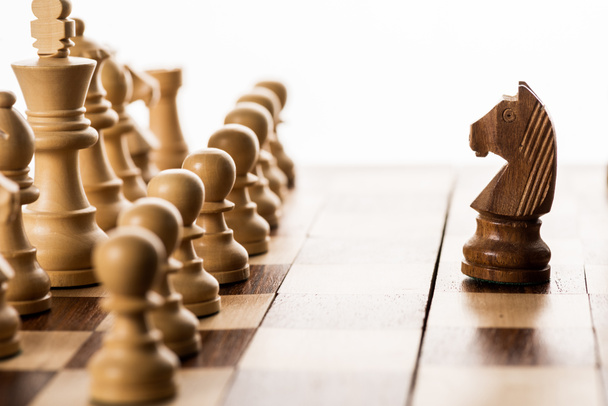 Selective focus of brown knight against chess pieces on chessboard isolated on white - Photo, Image