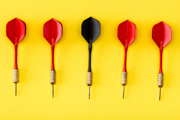 Flat lay with black dart among red on yellow  - Photo, Image