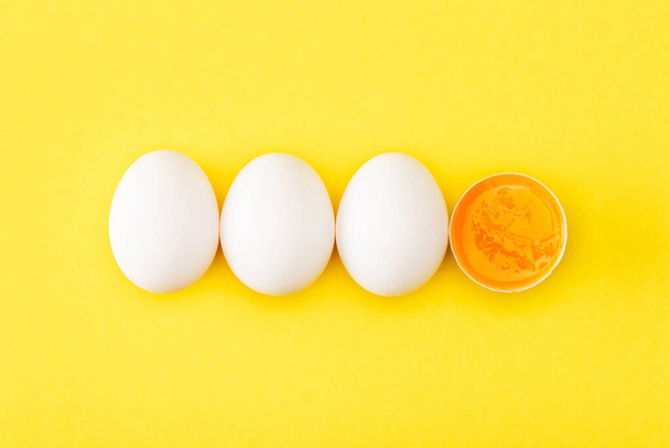 Κάτοψη του μισού ωμού αυγού μεταξύ ολόκληρων αυγών σε κίτρινο φόντο - Φωτογραφία, εικόνα