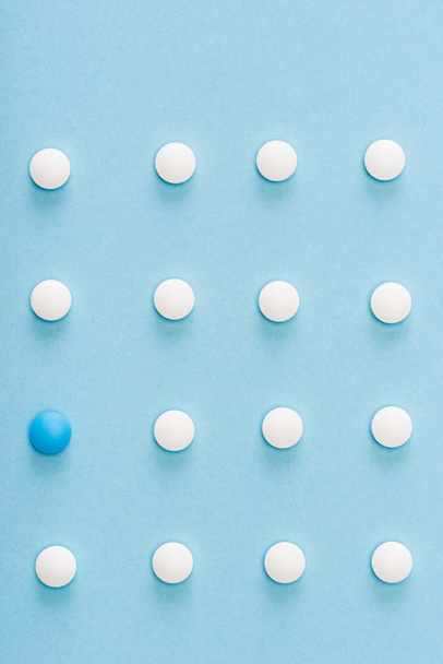 Flat lay with unique pill among white on blue background - Foto, Bild