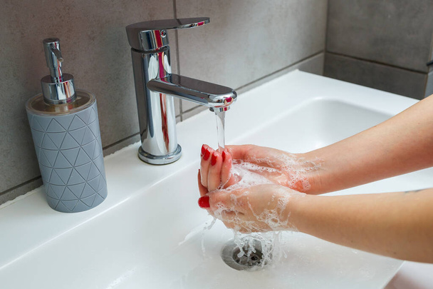 バスルームには銀製の蛇口が付いています。手のための液体石鹸で灰色缶。水道水をオンにすると、個人的な手の衛生。流水下での手洗い - 写真・画像
