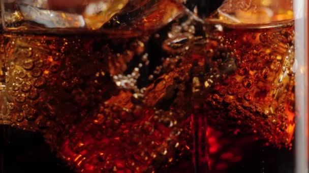 Camera moves up from ice cubes with bubbles in a glass of cola with black straw and brown highlights against black background. Concept of drinking coke or soda, relax and having fun. Close up. 4K - Filmmaterial, Video