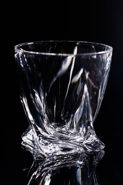 Black background stands a clean glass with reflection on a glass table. Facets on a Glass Cup - Foto, Imagem