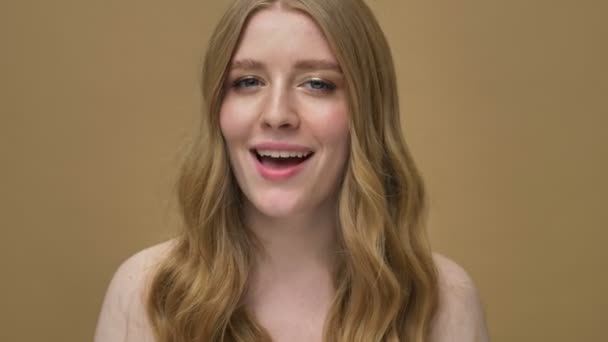 A happy smiling young half-naked woman with long hair is winking to the camera isolated over beige background - Séquence, vidéo