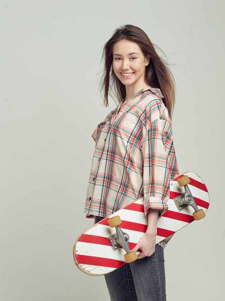 Cool girl student in casual clothes learns to ride a skateboard after classes at the University. - 写真・画像