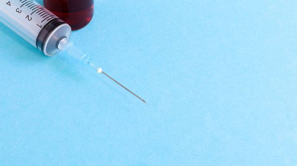 One medical glass bottle with red potion on a blue background and a medical disposable syringe with a needle. Medical concept shows a medical test tube and vaccines against coronavirus. Copy place. - Foto, immagini