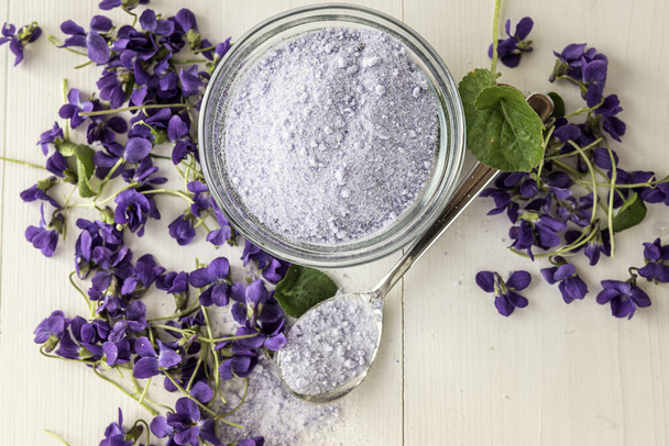 viola violeta γλυκό λιλά κρύσταλλα ζάχαρης για τη διακόσμηση κέικ ψησίματος, κοντά σε φρέσκα άνθη λουλουδιών viola violetta odorata τσάι με βιόλα σιροπιού βιόλα λιλά ζάχαρη κρύσταλλα - Φωτογραφία, εικόνα