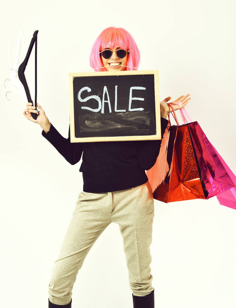 girl in wig holding package, hangers, board with sale inscription - Zdjęcie, obraz
