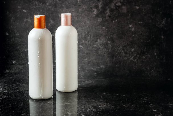 Three white bottles with shampoo, shower gel and body balm, care. Copyspace on a black stone background. - Photo, Image