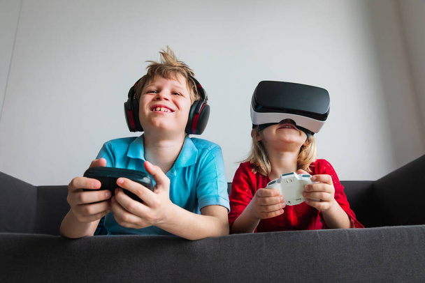 dzieci grające w gry wideo w domu, chłopiec i dziewczyna z pilotami w pomieszczeniach - Zdjęcie, obraz