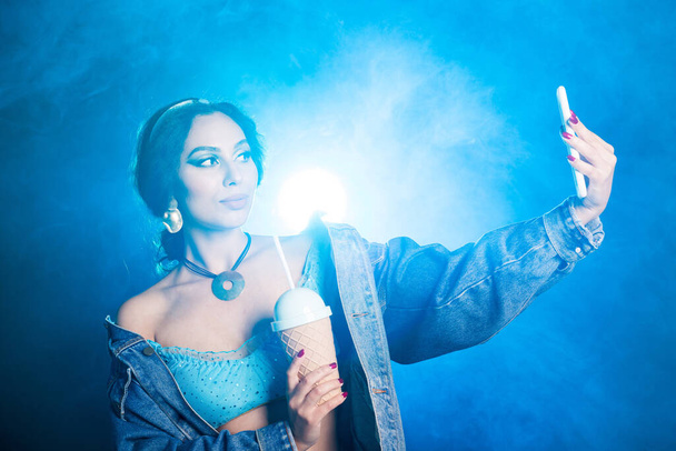 Concetto magico, cosplay e fiaba - Ritratto di una giovane donna a immagine di una principessa delle fate orientali prende selfie su sfondo blu
. - Foto, immagini