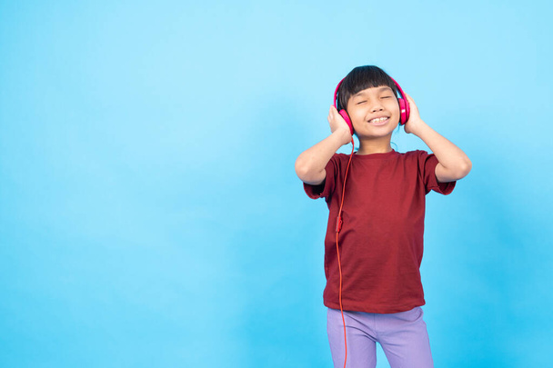 Thai Asia girl kid listening music, wearing phink earphone on blue studio on blue background  - Photo, Image
