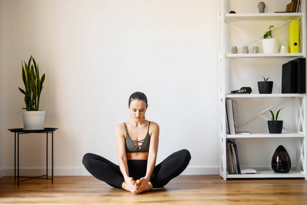 Young positive woman is practicing yoga at home - 写真・画像