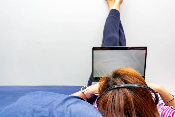 Девушка, работающая из дома на кровати с ноутбуком и наушниками. Мама работает из дома во время пребывания дома уведомление из-за вспышки вируса
 - Фото, изображение