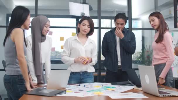 Jovens empresários asiáticos felizes e mulheres de negócios encontrando ideias de brainstorming sobre novos colegas de projeto de papelada trabalhando juntos planejando estratégia de sucesso desfrutar de trabalho em equipe em pequeno escritório moderno. - Filmagem, Vídeo