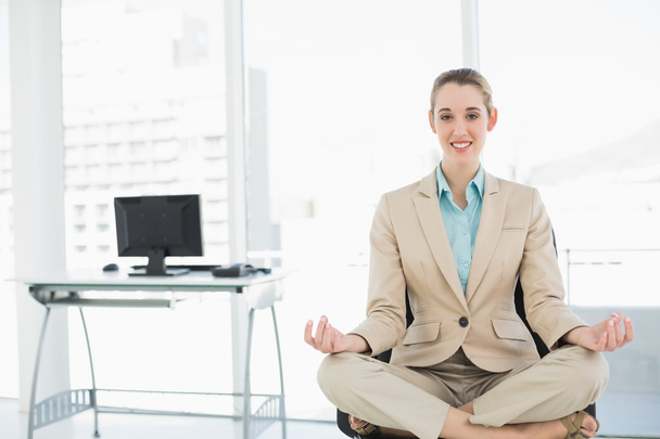 Beautiful calm woman sitting in lotus position on her swivel chair - Foto, Imagen