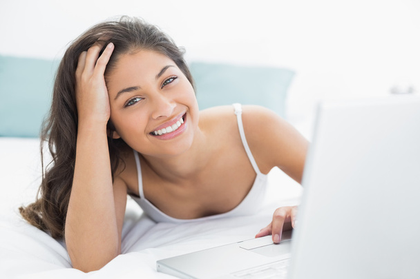 Smiling casual woman using laptop in bed - Фото, зображення