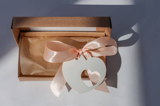 Karton paket sonrası kalp kartı etiketi beyaz arka planda yaratıcı minimalizm tarzında doğal gölge. Kahverengi eko hediye kutusu, çevrimiçi alışveriş konsepti. Zıpla süper satış, indirimli etiket özel bayrağı - Fotoğraf, Görsel