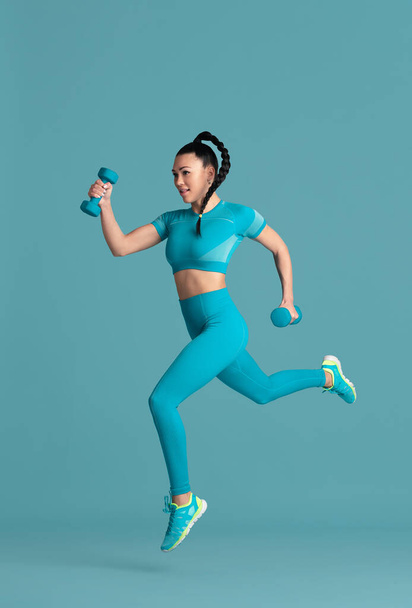 Beautiful young female athlete practicing on blue studio background, monochrome portrait - Fotó, kép