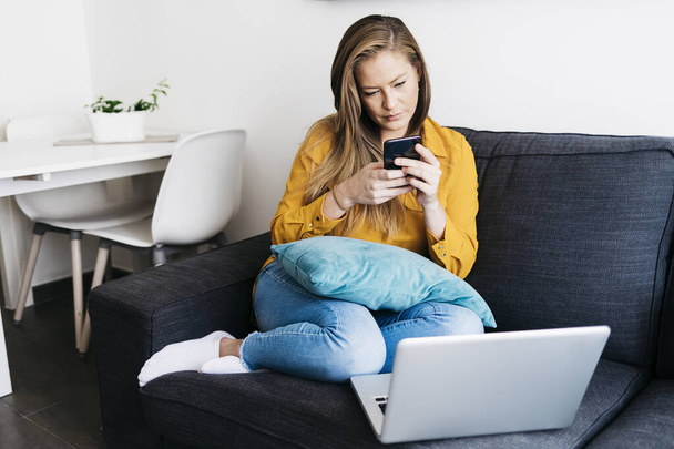 Beautiful adult woman sitting on sofa while using smartphone - Foto, afbeelding