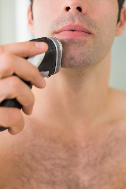 Smiling handsome shirtless man shaving with electric razor - Photo, image
