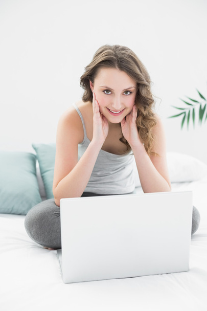 Smiling casual brunette using laptop in bed - Photo, Image