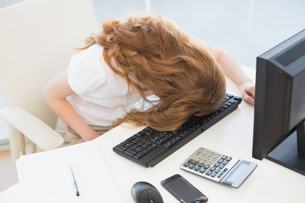 Businesswoman resting head on keyboard in office - Foto, afbeelding