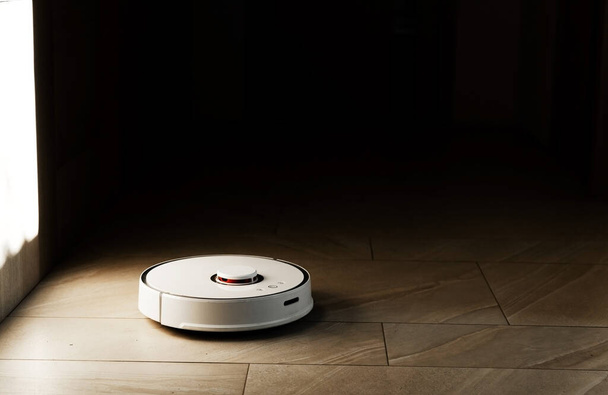 Robot vacuum cleaner during cleaning,white robot vacuum cleaner cleans the floor from debris,home cleaning with an electric vacuum cleaner,vacuum cleaner electric robot cleaning technology - Фото, зображення