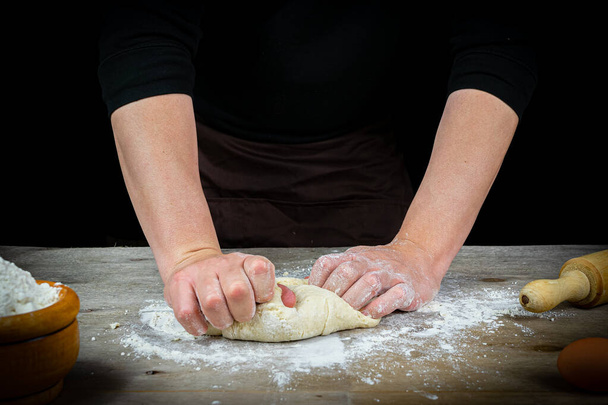 Mãos de homem amassando a massa de pão em uma mesa de madeira com fundo preto. Conceito de artesanato
 - Foto, Imagem